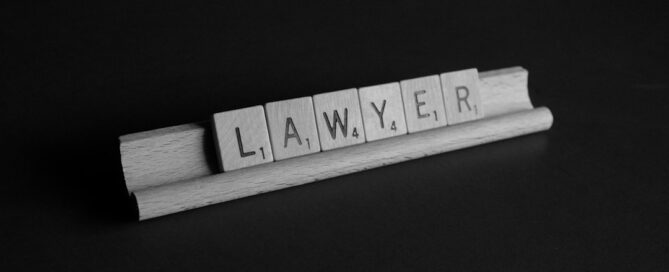 Wooden Scrabble tiles on a rack spell the word "LAWYER" against a dark background.