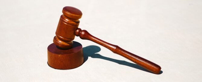 A wooden gavel rests on a matching round base, symbolizing law and justice, against a plain white background.