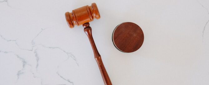 A wooden judge's gavel and sound block rest on a light-colored, marbled surface.