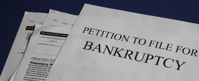 A stack of documents on a dark blue surface, with the top document titled "Petition to File for Bankruptcy.