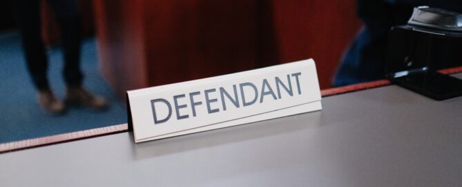 A sign labeled "Defendant" placed on a desk in a courtroom setting.