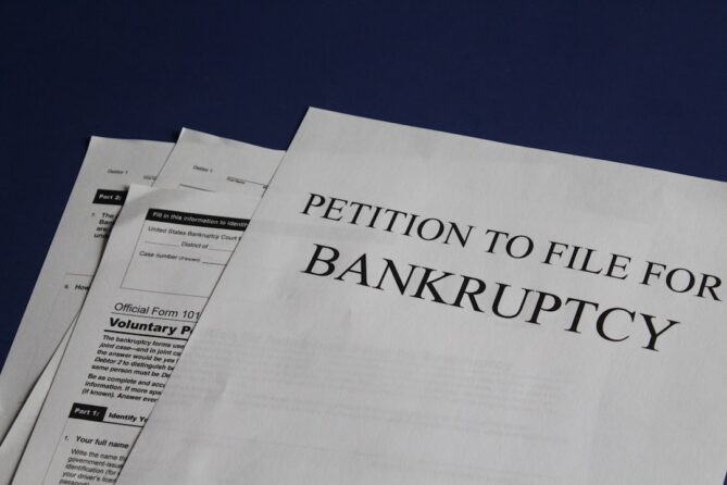 Several documents, including one titled "Petition to File for Bankruptcy," are arranged on a dark blue surface.