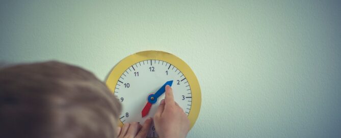 A child adjusts the hands of a toy clock on a light-colored wall.