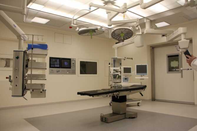 A modern, sterile operating room equipped with advanced medical equipment, surgical table, multiple monitors, overhead lights, and various apparatuses for surgical procedures.