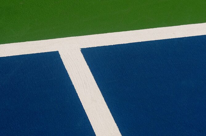 A section of a sports court featuring the intersection of blue and green surfaces with a white boundary line.