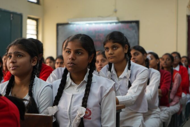 Students in school uniforms, seated in a classroom and attentively looking forward.