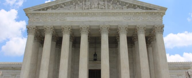 The front facade of the United States Supreme Court building with a row of large columns and a sculpted frieze, set against a partially cloudy sky.